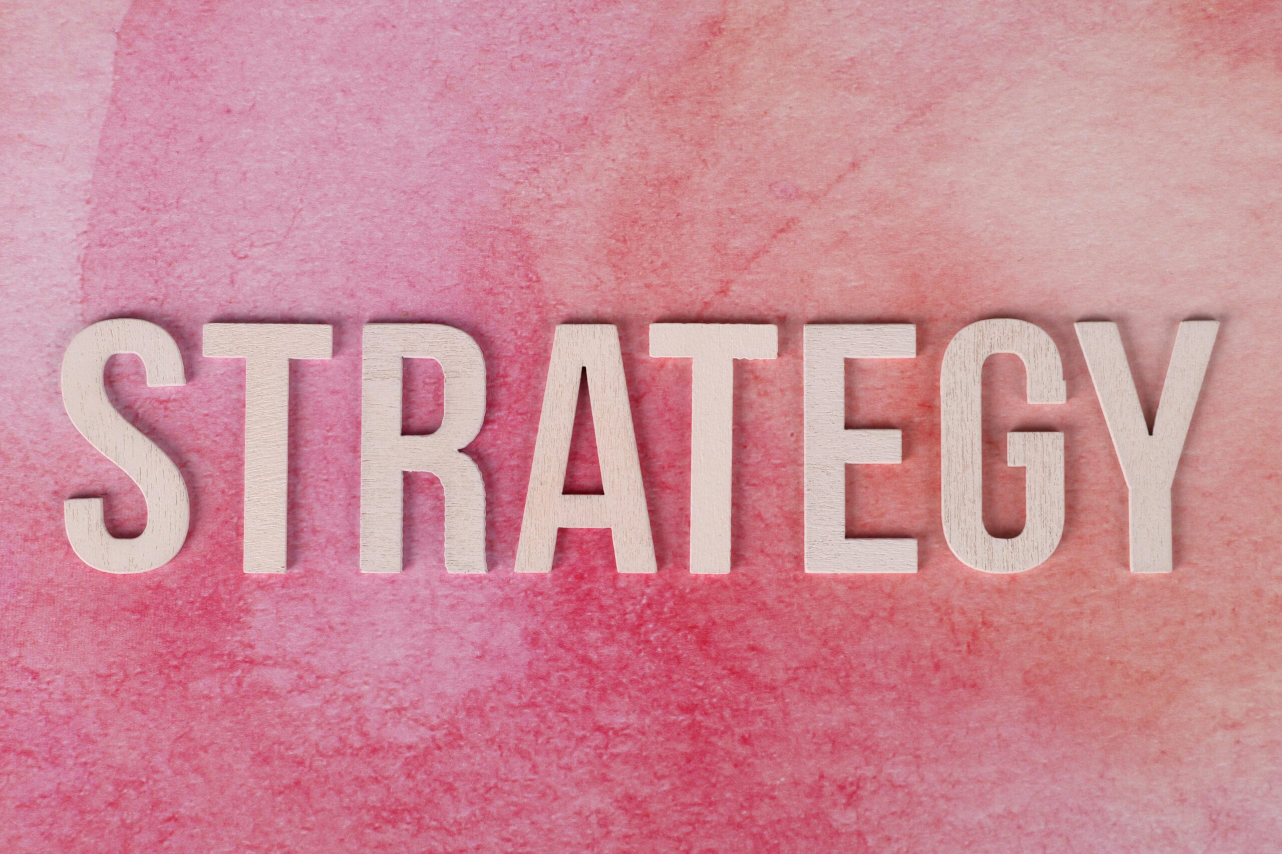 pexels-photo-33137134-33137134 Wooden letters spelling 'Strategy' on a pink textured background.