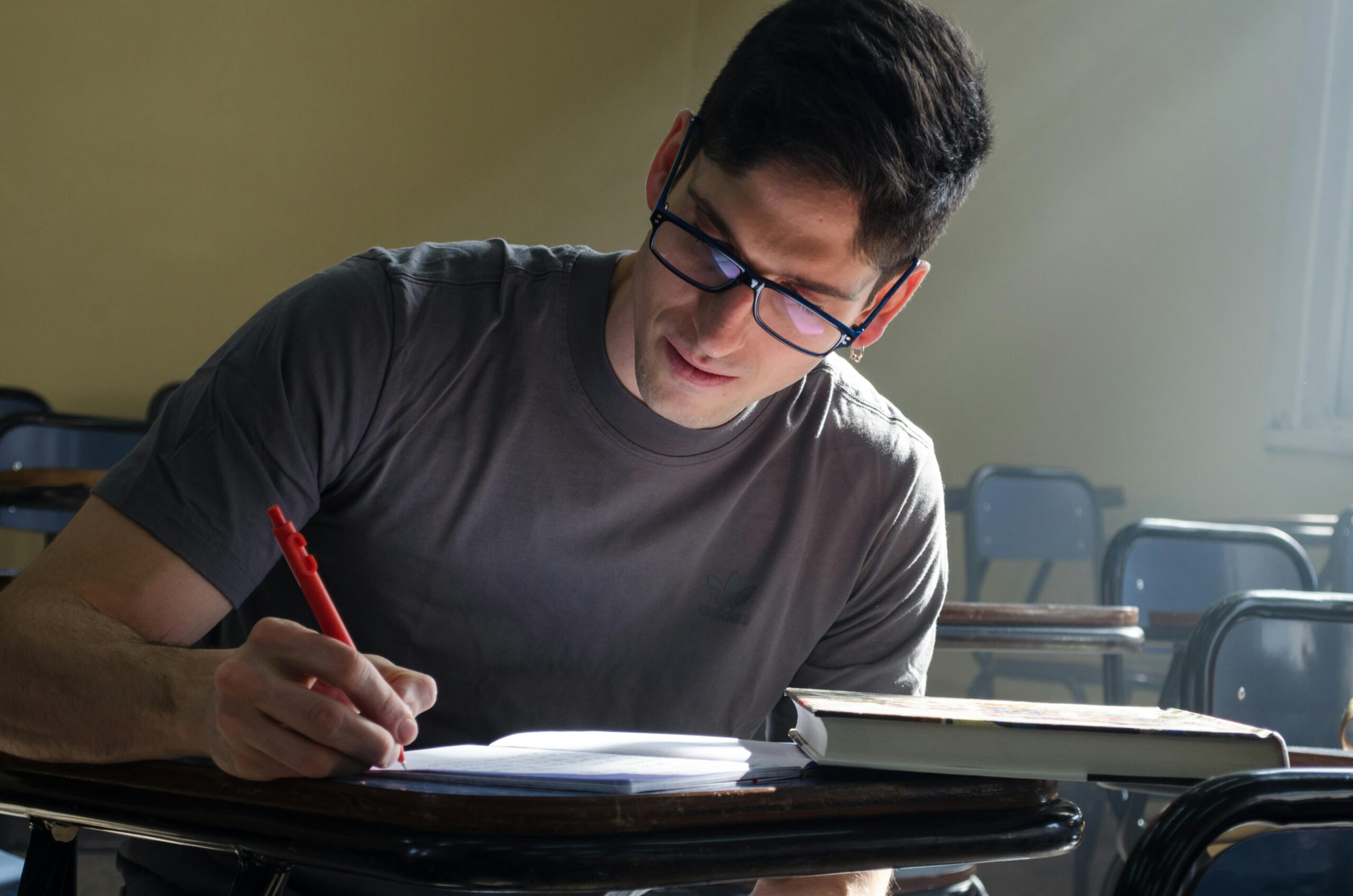 Focused student studying at a desk in a classroom with natural light streaming in.